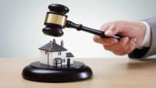 Online auctions company auctioneer holds wooden gavel over small plastic model house