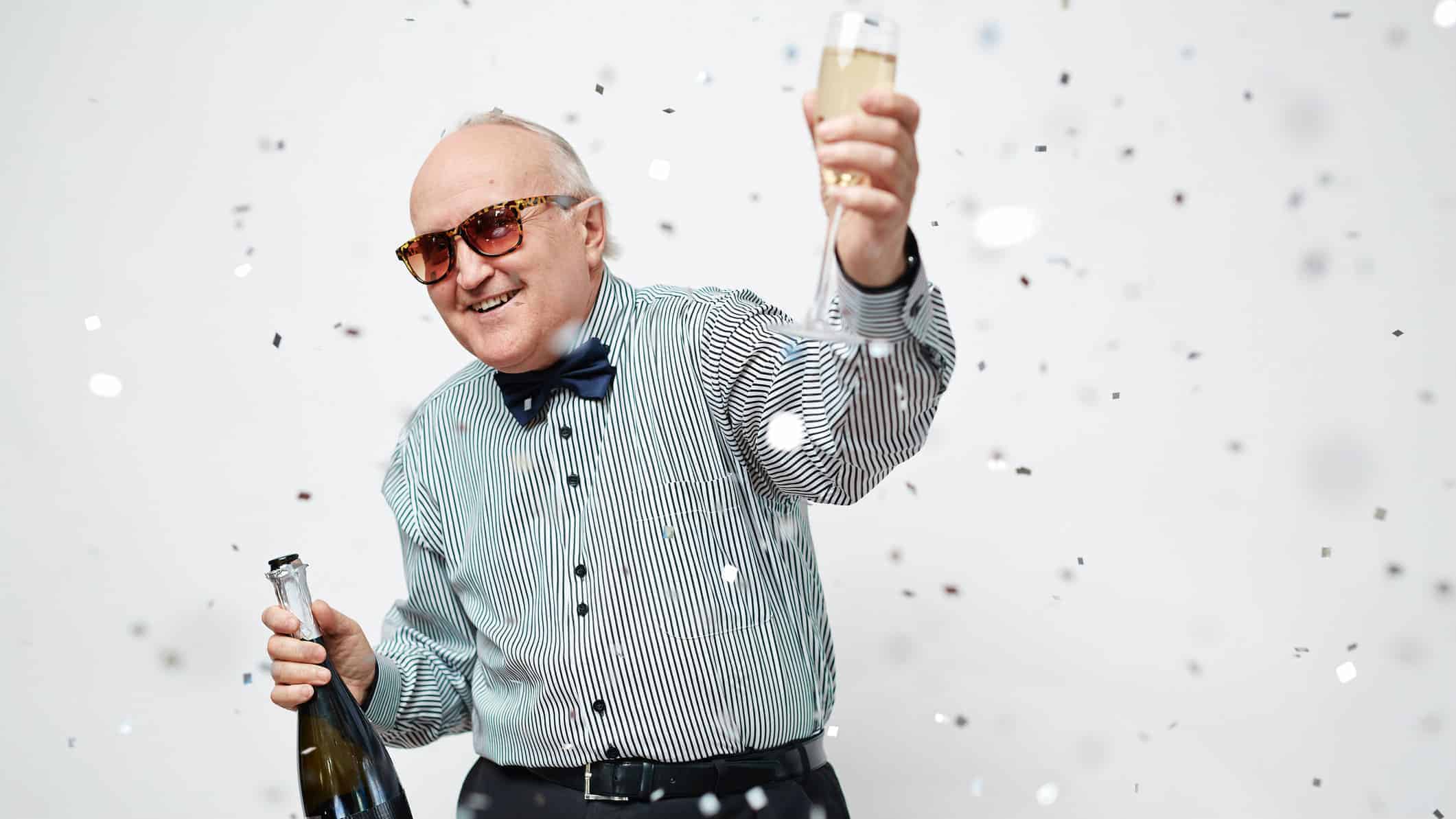 older man holding up a glass of champagne in celebration