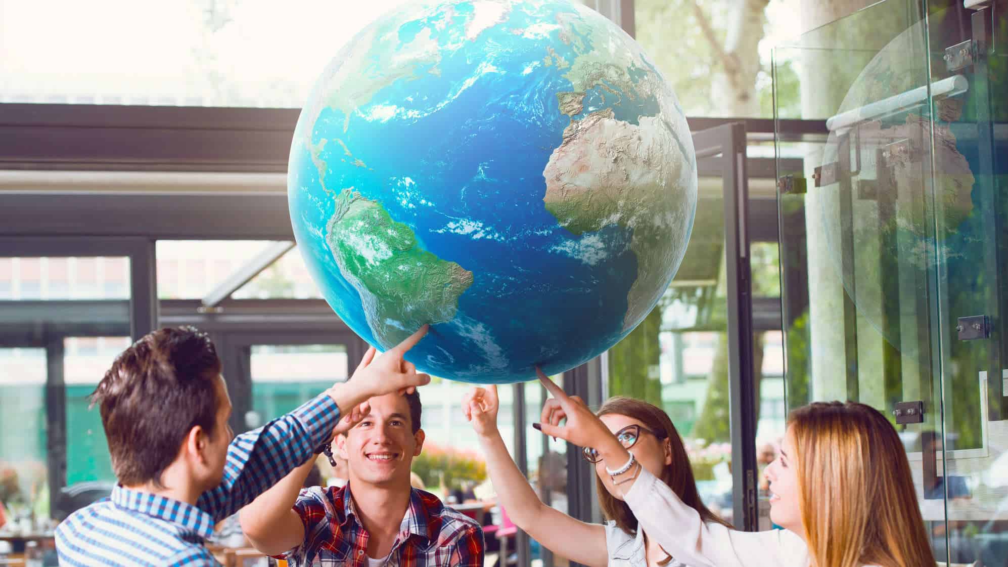 a group of people hold up a large globe above their heads.
