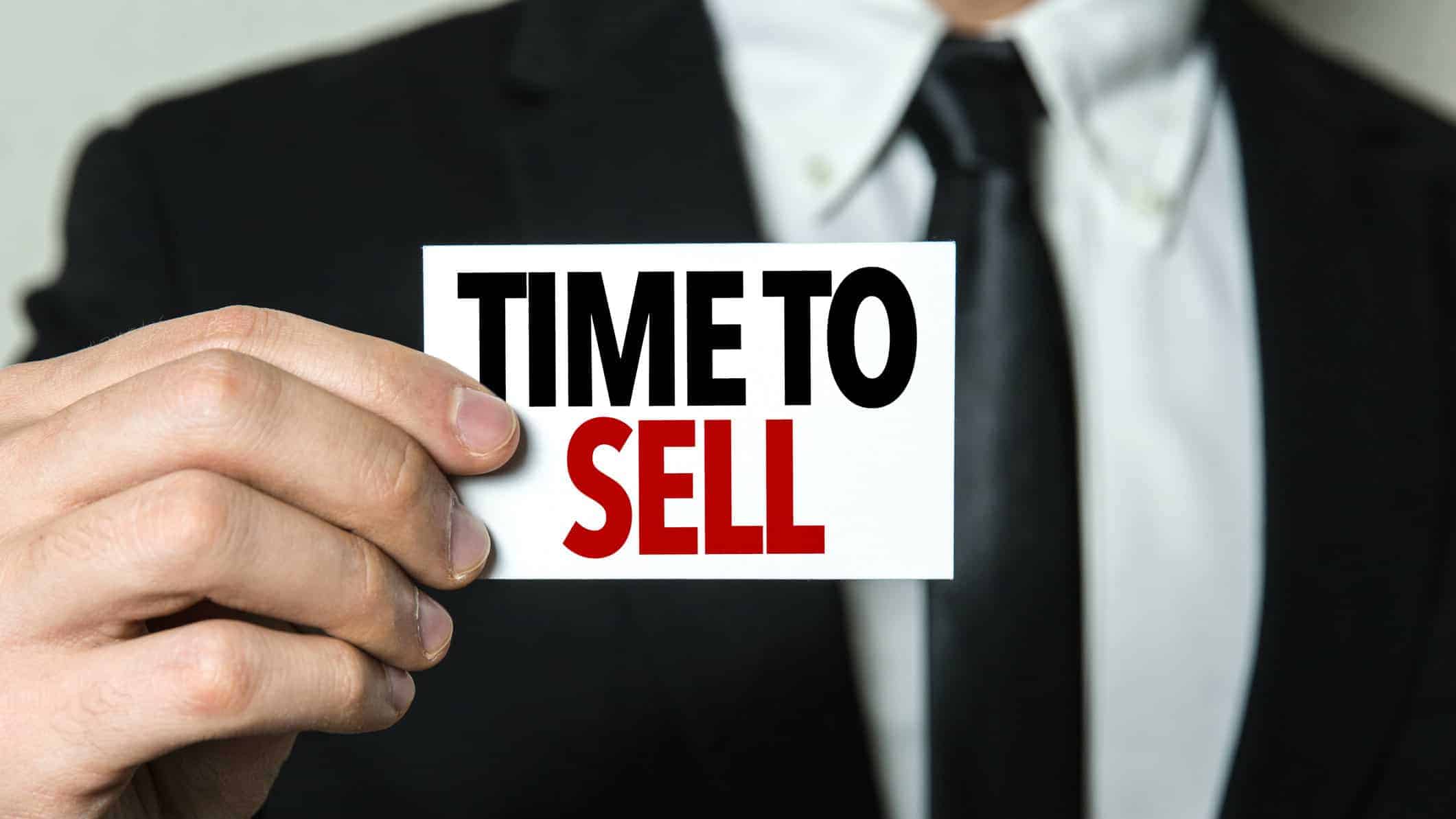 business man holding sign stating time to sell