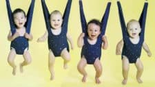 Four babies in bouncing harnesses look adorable as they smile at the camera in a line together.