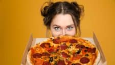 Woman holding Domino's pizza up to her face and looking excited about the company's latest news