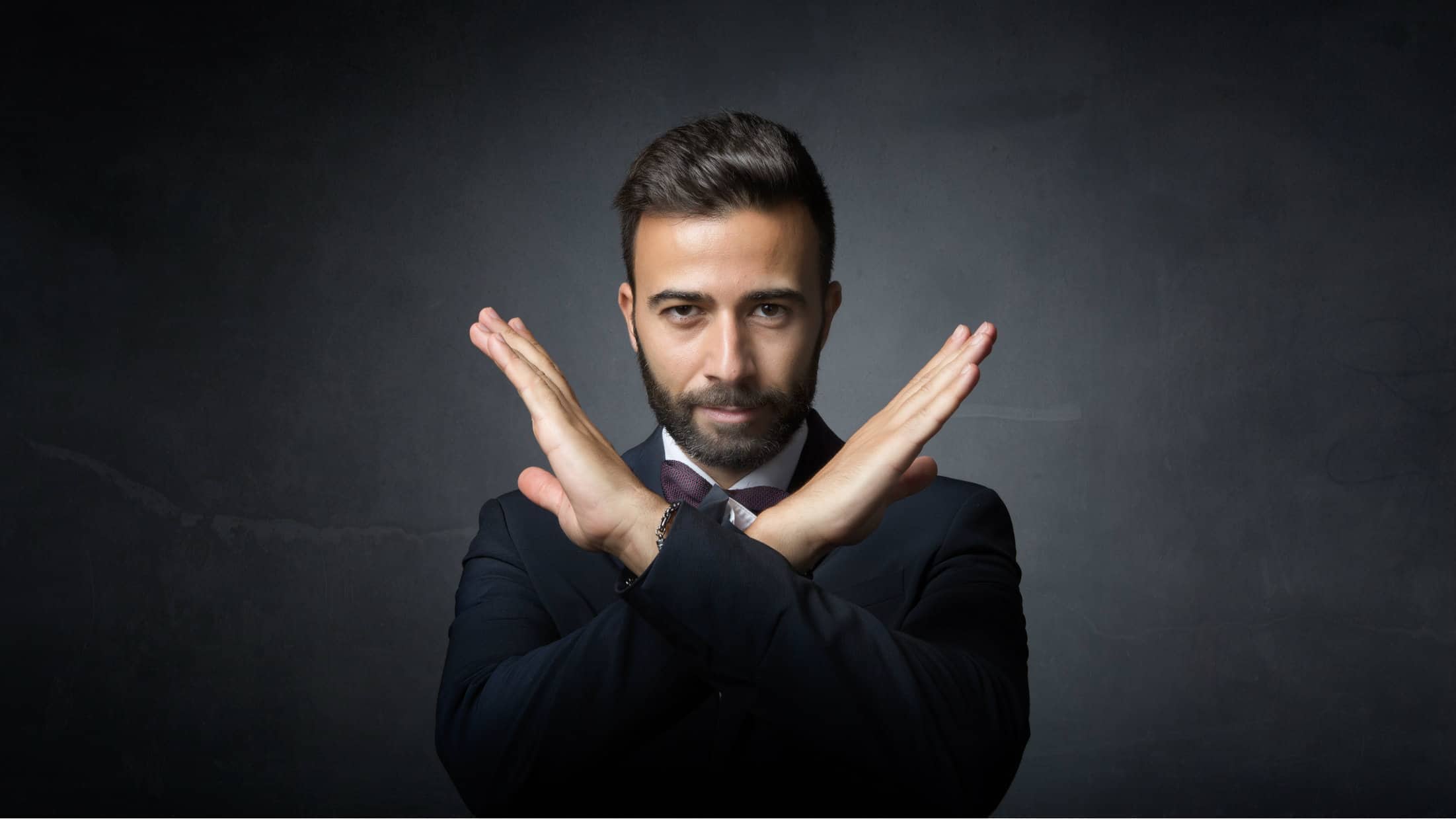 A man stands with his arms crossed in an X shape in front of him, indicating no deal.