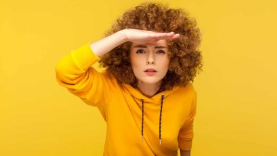 a woman leans forward with her hands shielding her eyes as if she is looking intently for something.