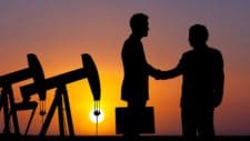 The shadows of an oil rig and two businessmen shaking hands with a sunset backdrop