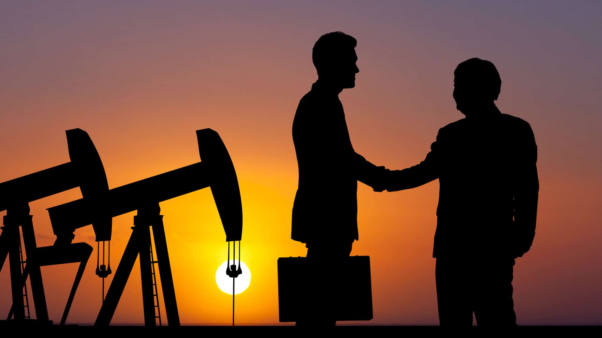 The shadows of an oil rig and two businessmen shaking hands with a sunset backdrop