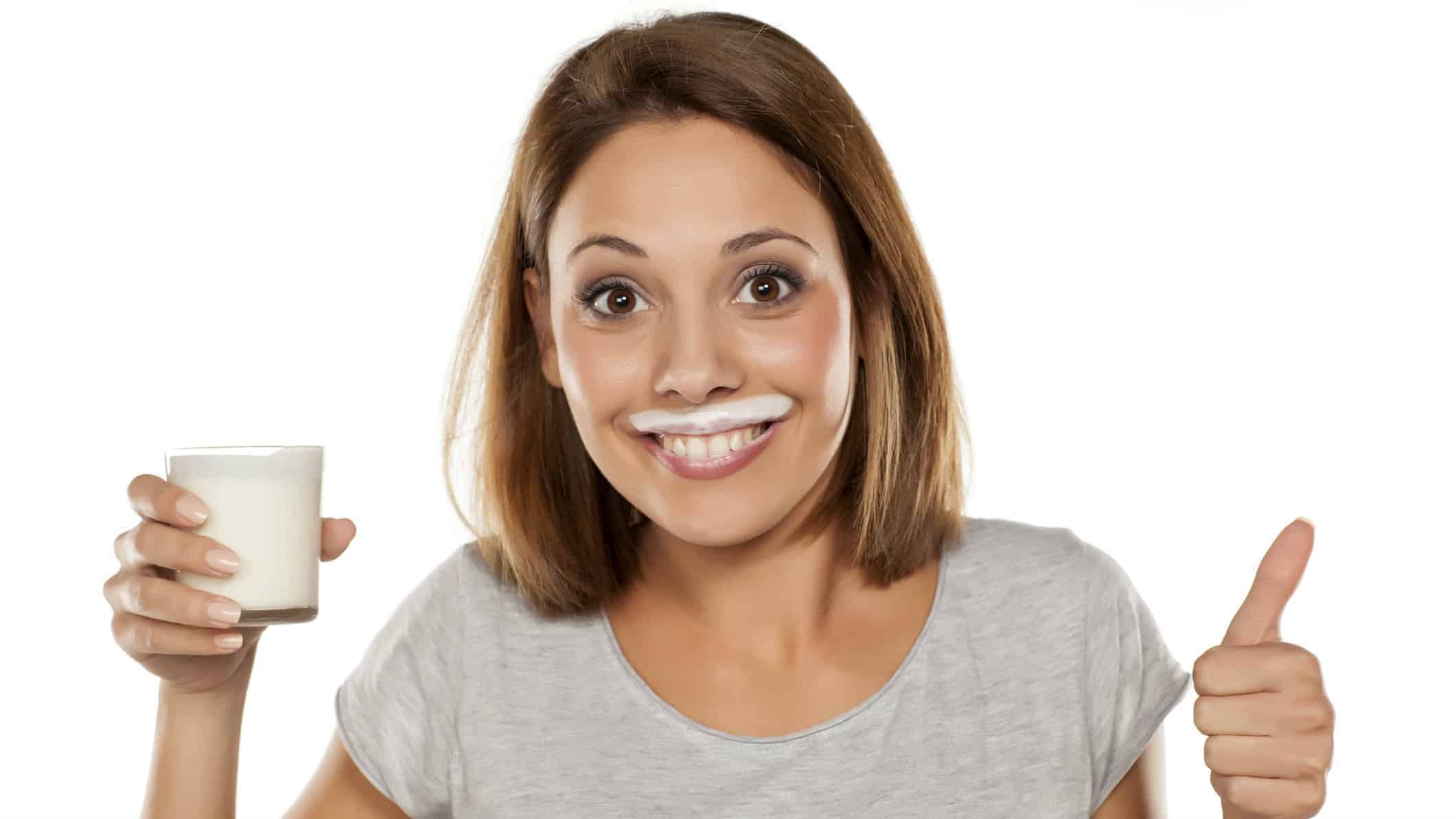 woman with milk moustache holding glass of milk and giving thumbs up representing a positive share price