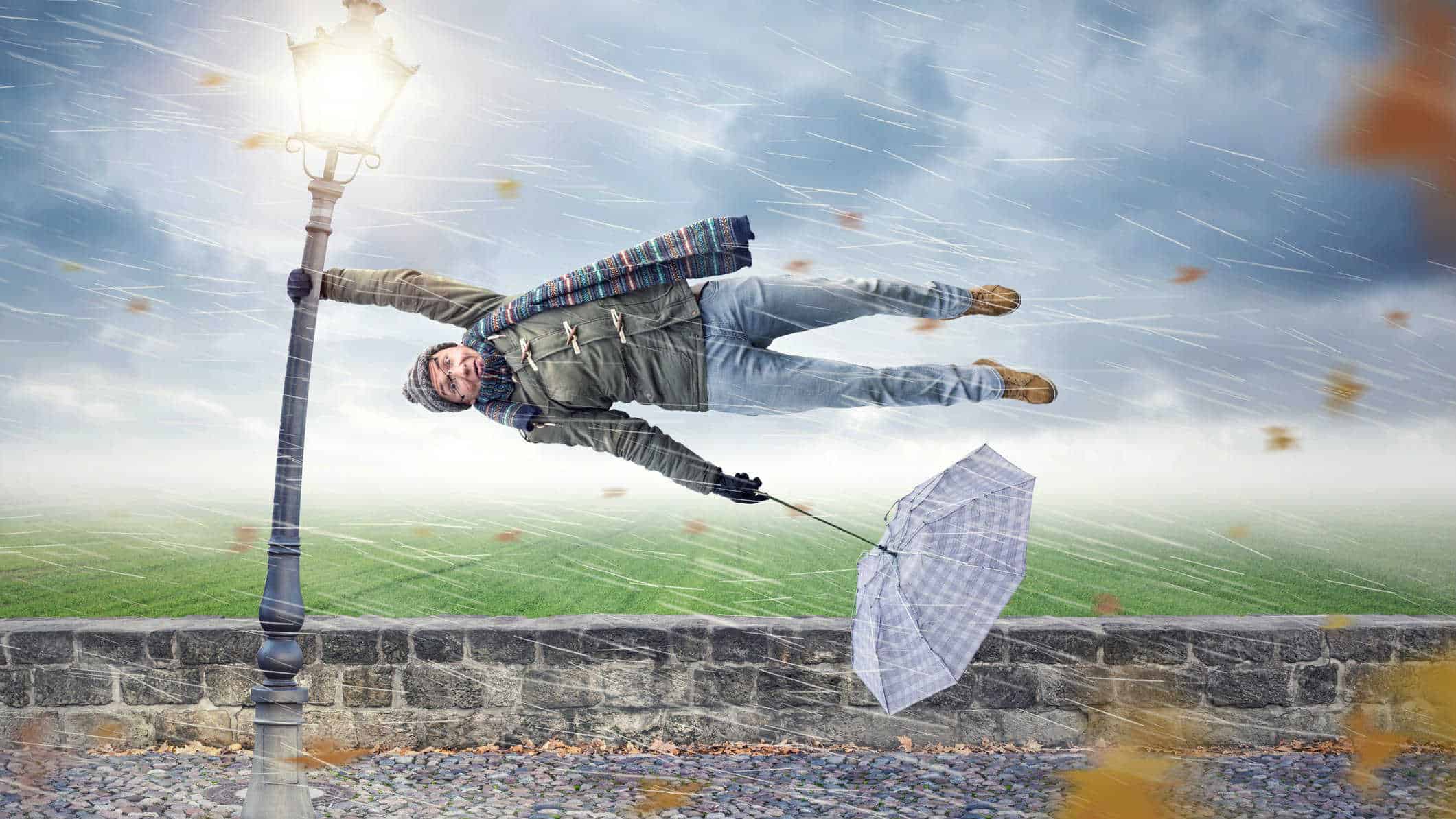 falling asx share price represented by man holding onto pole getting blown in the wind