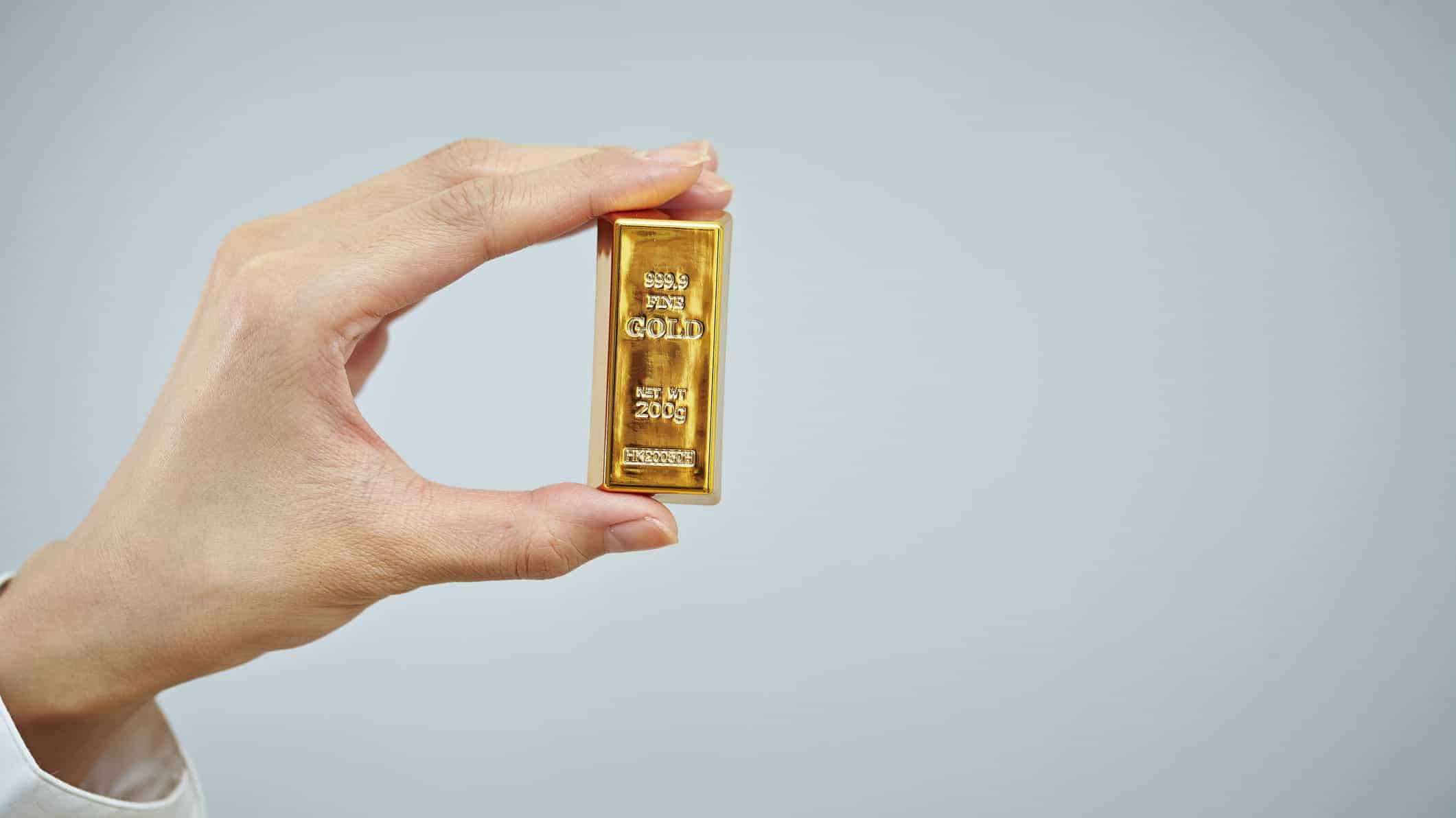 Hand holding solid gold bar in front of neutral background