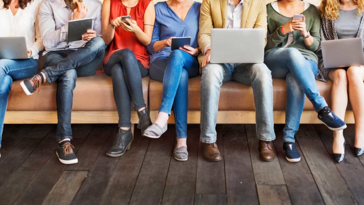 A row of 6 ASX investors sitting on a couch trading ASX 200 shares using various devices phones and laptops trading shares
