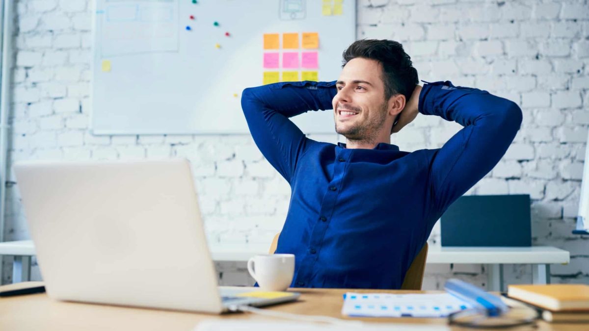 Smiling office man leaning back in chair in front of laptop