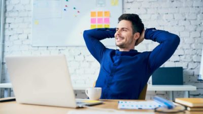 Smiling office man leaning back in chair in front of laptop