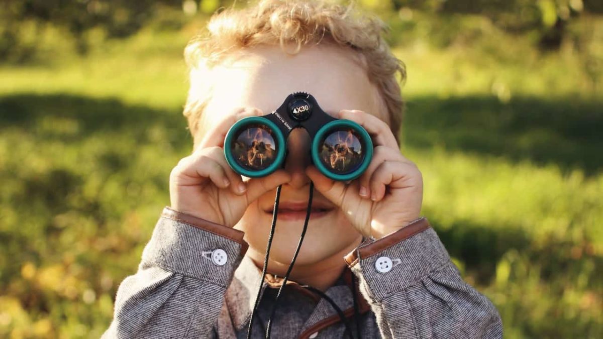 Boy with small binoculars and green field in background