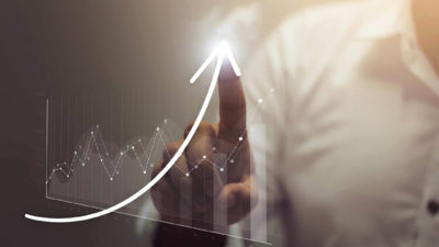 Pointing to an upward trend in data on screen.