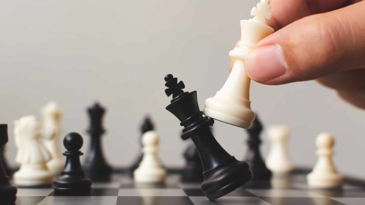 ASX share price moves represented by chess board with person knocking over black piece with white piece