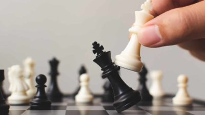 ASX share price moves represented by chess board with person knocking over black piece with white piece