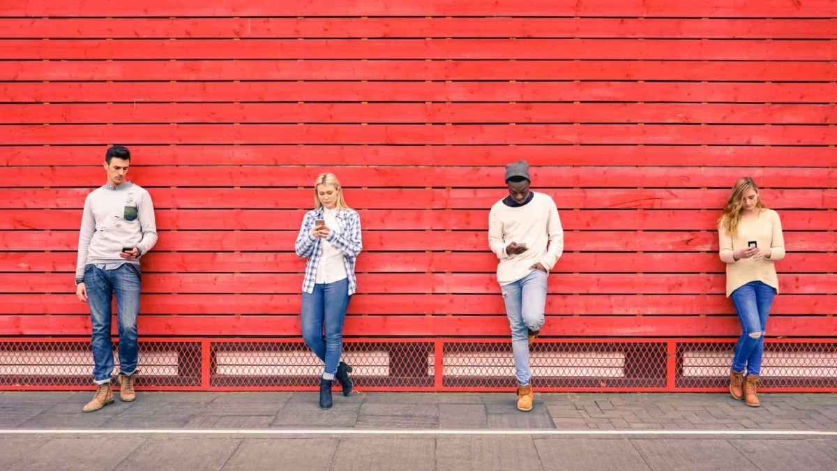 group of young people standing against red wall using their smart phones