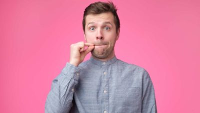 Man in button up shirt miming a secret in front of pink background