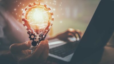 hand holding light bulb next to laptop