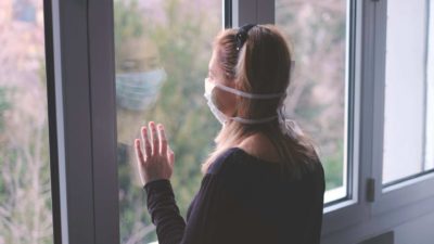 woman wearing mask looking out window