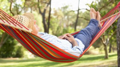 Retired man reclining in hammock with feet up, retire early