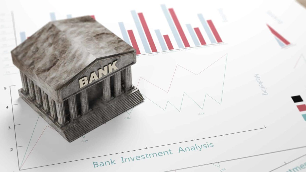 Small grey plastic model of a bank building on top of a piece of paper with a performance chart showing red and blue columns