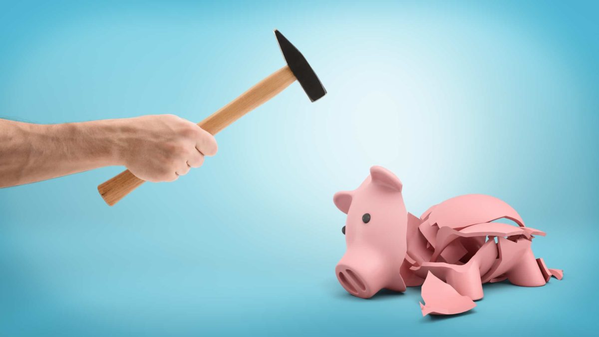 hand holding hammer smashing open empty piggy bank