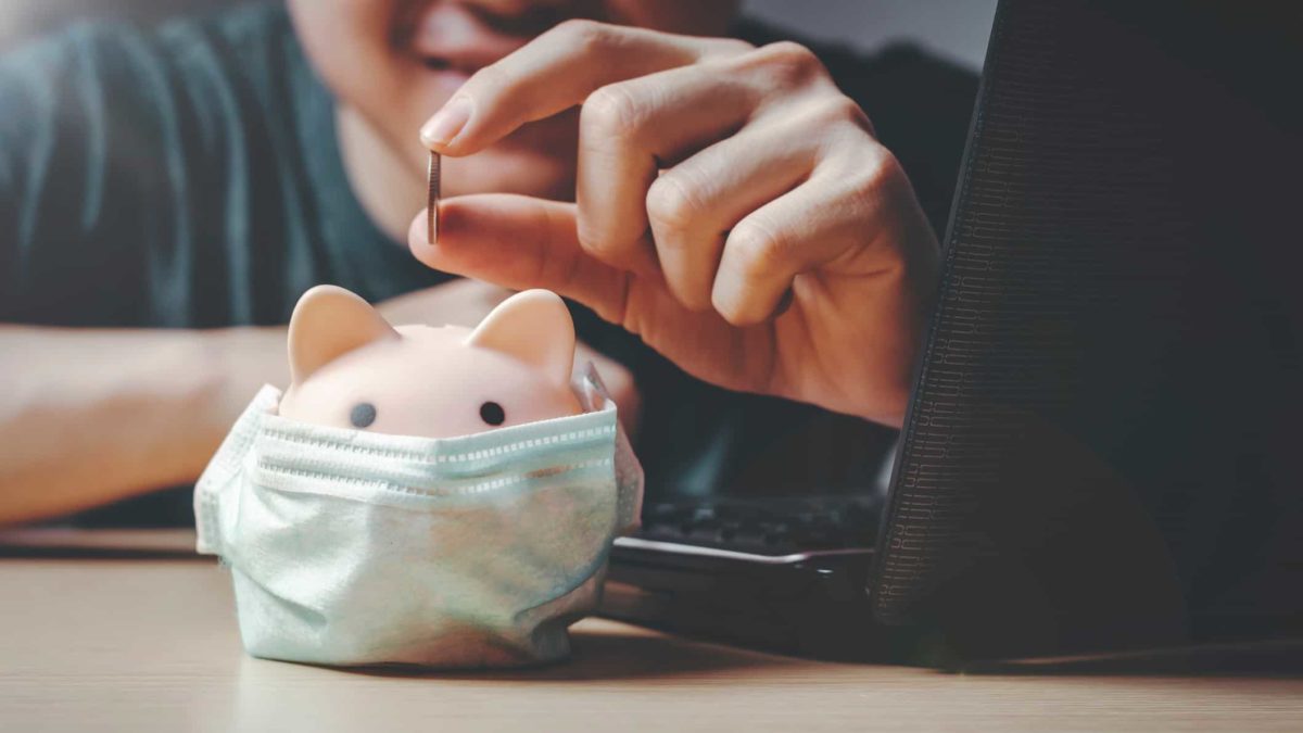 man putting coin in piggy bank that's wearing covid mas representing asx shares to hold during covid