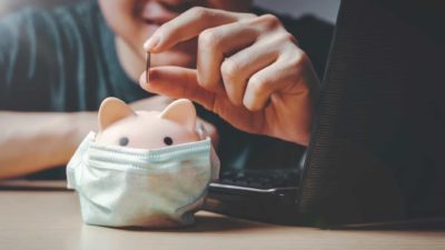 man putting coin in piggy bank that's wearing covid mas representing asx shares to hold during covid