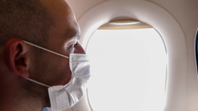 airline passenger wearing face mask looking out plane window representing flight centre share price on watch