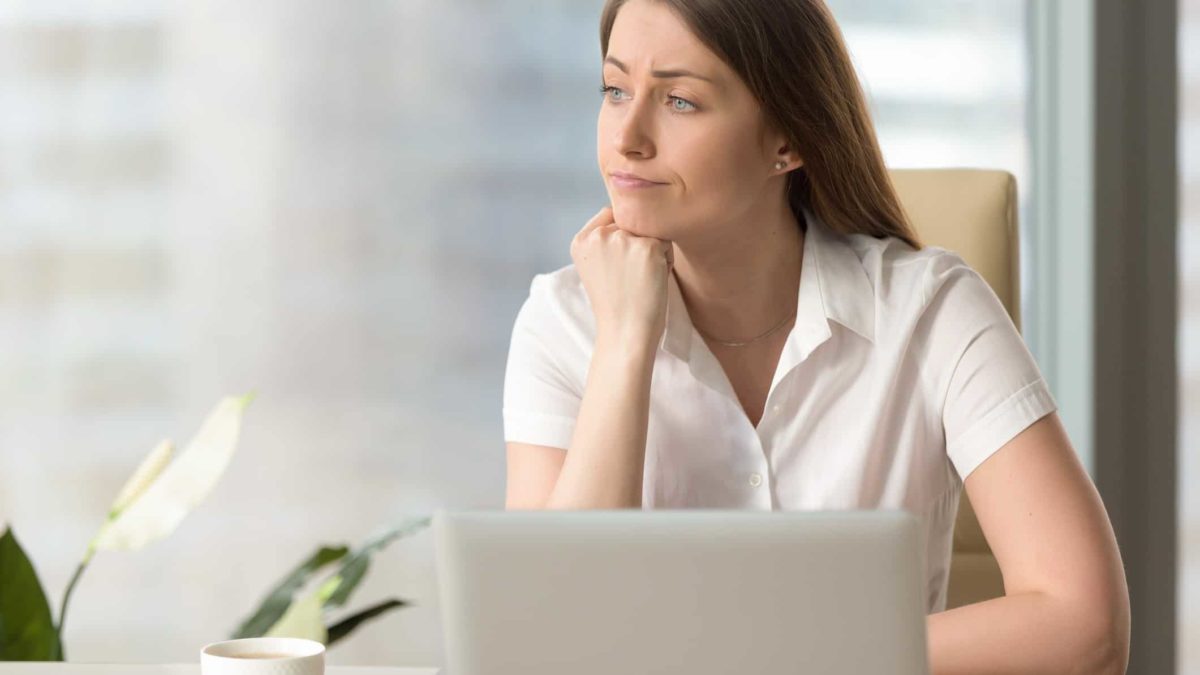 A woman sits at her desk in front of her laptop and looks away feeling disappointed with today's share price falls
