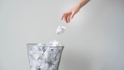 Hand throwing scrunched up paper in rubbish bin