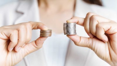 woman holdings small pile of coins representing brainchip share price and larger pile of coins
