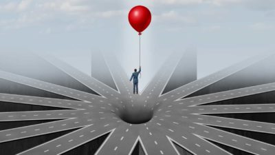 man suspended in air over hole in the road by holding a balloon representing pitfalls of infrastructure investments