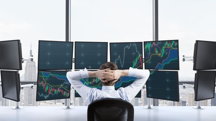 Investor sitting in front of multiple screens watching share prices