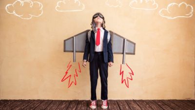 Young girl wearing a suit and tie with rocket wings looks to the sky representing the highest traded stocks today