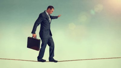 A man in a suit carrying a briefcase carefully keeps his balance while he walks a tightrope.