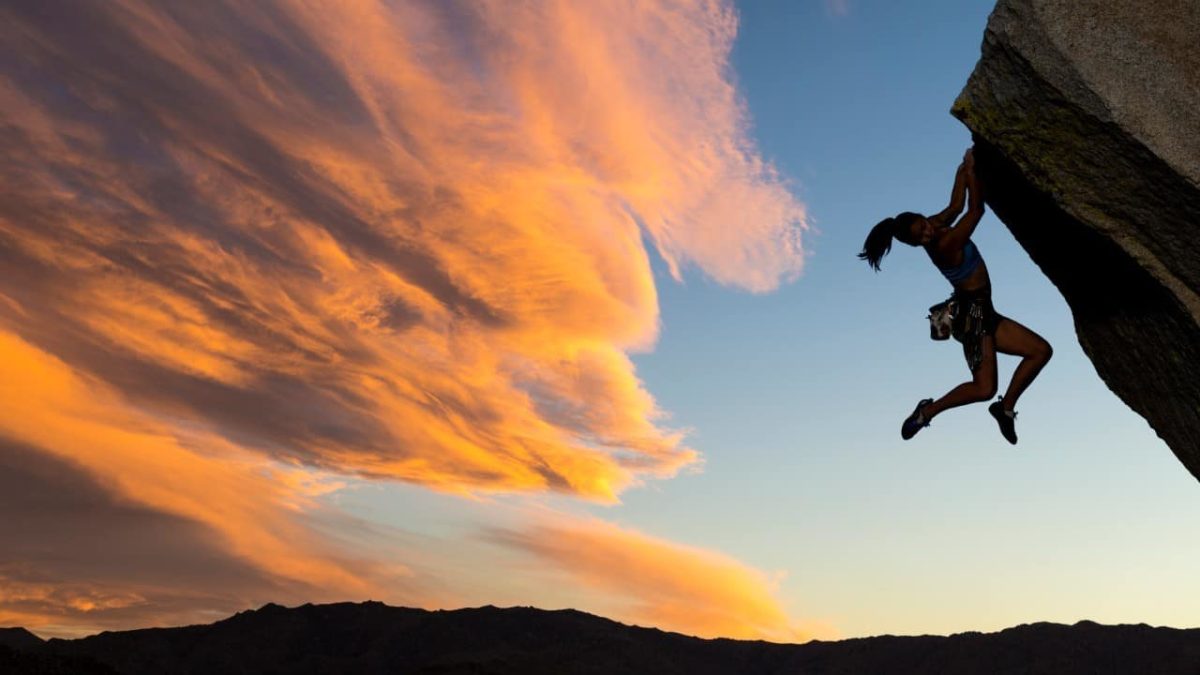 Climber hanging onto to a cliff face, indicating a falling share price
