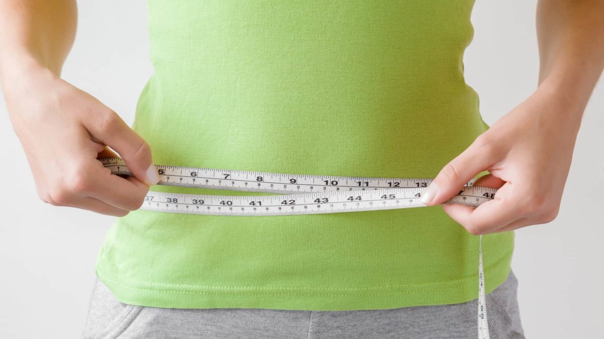 woman using tape measure to measure her waist size
