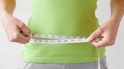 woman using tape measure to measure her waist size