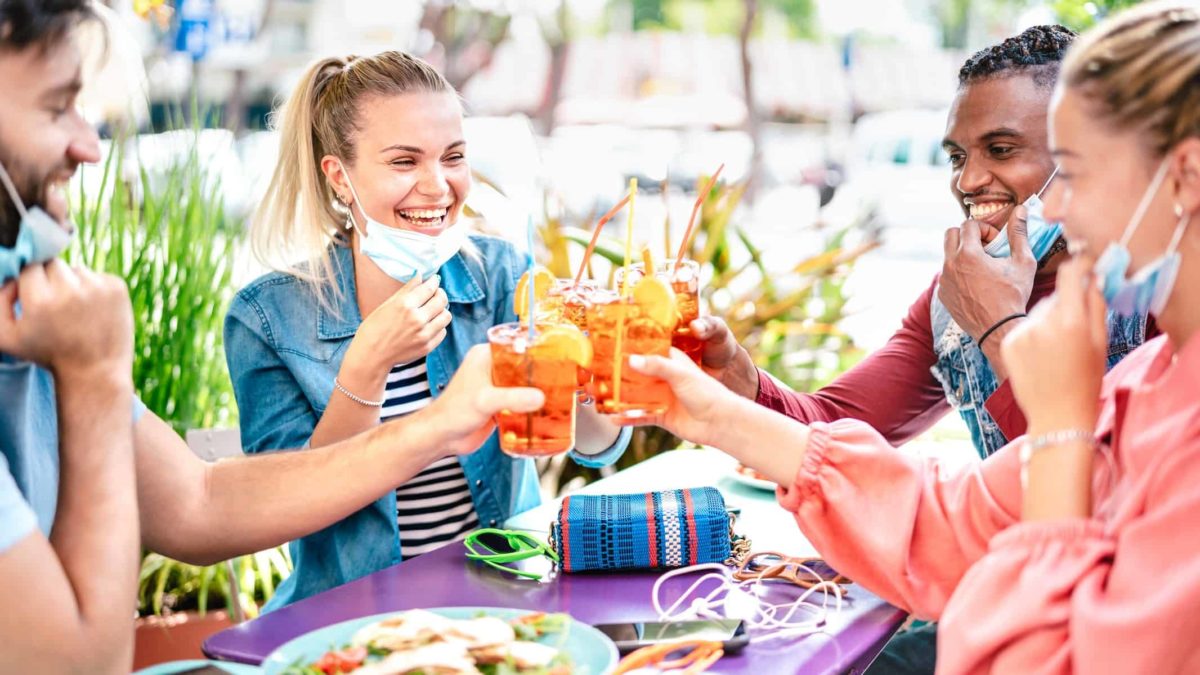 Group of young friends wearing facemasks dining out and raising glasses in a toast