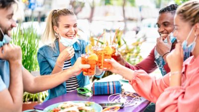 Group of young friends wearing facemasks dining out and raising glasses in a toast