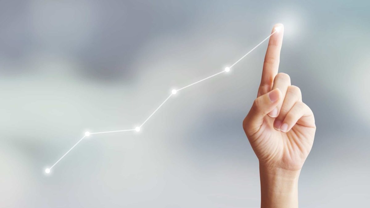 hand on touch screen lit up by a share price chart moving higher