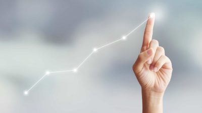 hand on touch screen lit up by a share price chart moving higher