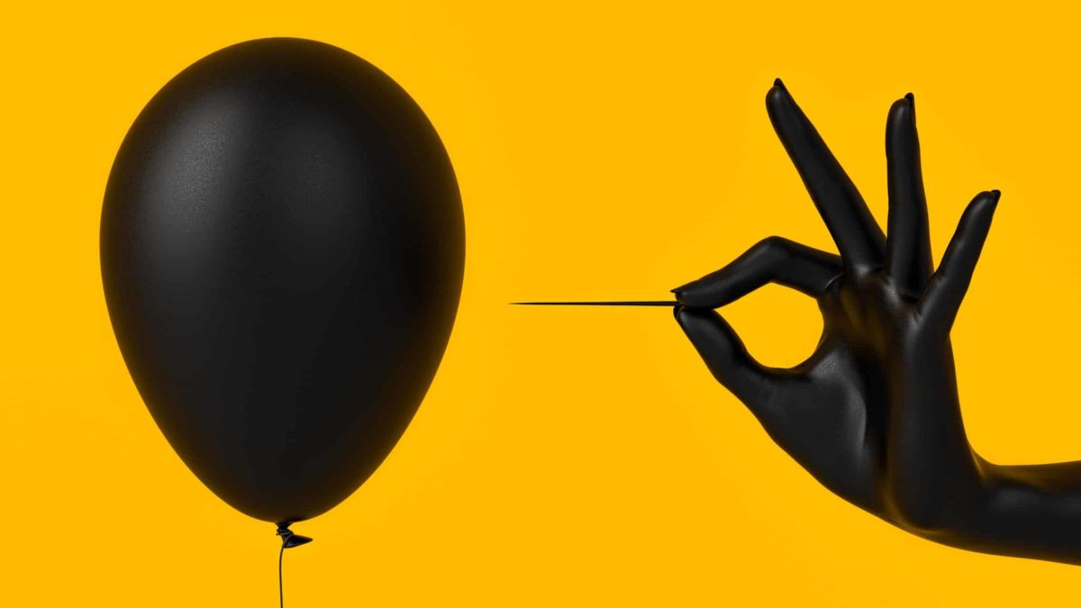A hand holding a pin about to burst a balloon, indicating a crash or drop in asx shares