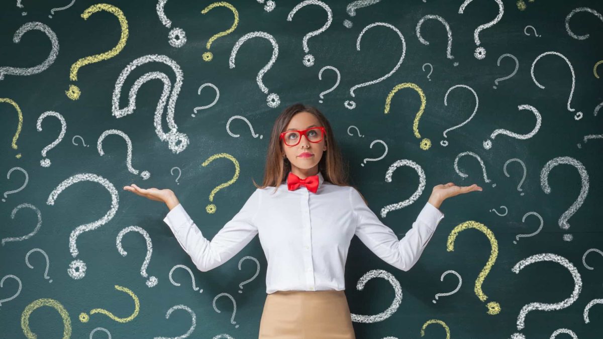 A teacher in front of a classroom chalkboard filled with questionmarks, indicating share market uncertainty
