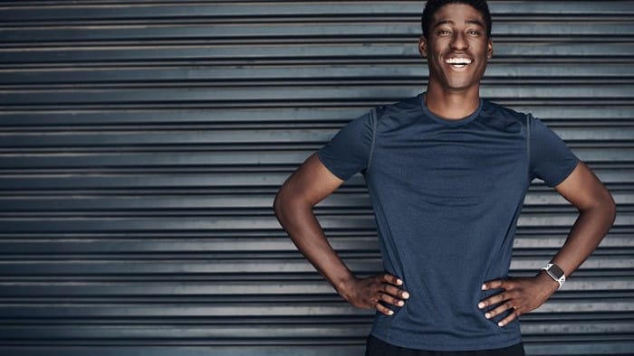 Man in activewear stands smiling in front of wall.