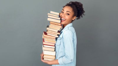 a smiling young woman carrying a pile of books, indicating a lifting share price for book sellers