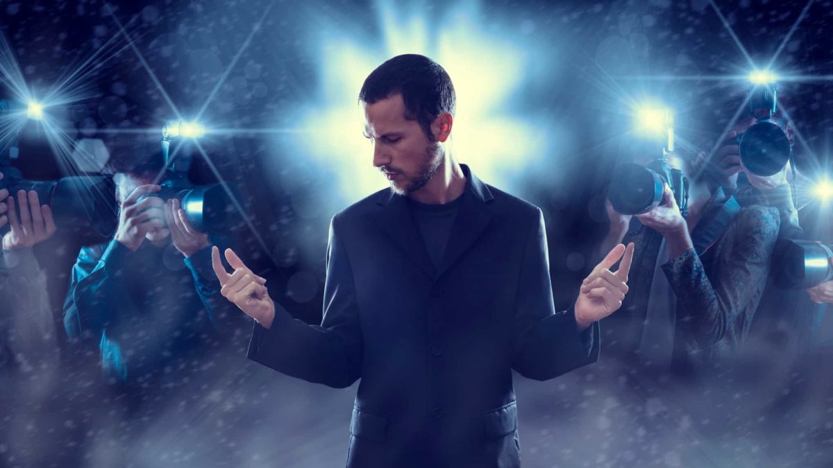 A rockstar stands bathed in the spotlight and camera flashes from photographers, indicating a the most popular and successful share on the market