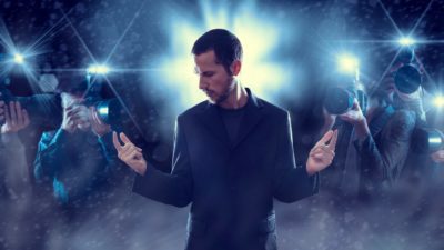 A rockstar stands bathed in the spotlight and camera flashes from photographers, indicating a the most popular and successful share on the market